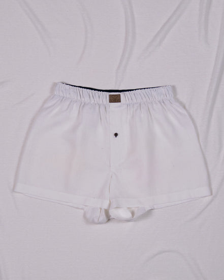 Weiße Herren Boxershorts aus Leinen mit Knopf und dunkelblauem Bund auf hellem Hintergrund