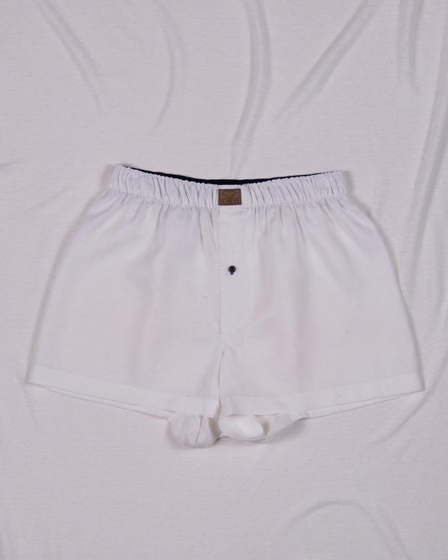 Weiße Herren Boxershorts aus Leinen mit Knopf und dunkelblauem Bund auf hellem Hintergrund