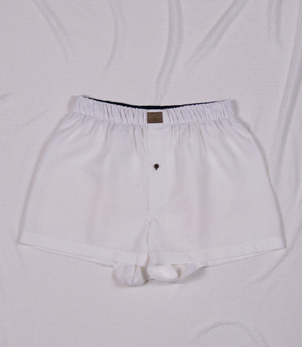 Weiße Herren Boxershorts aus Leinen mit Knopf und dunkelblauem Bund auf hellem Hintergrund
